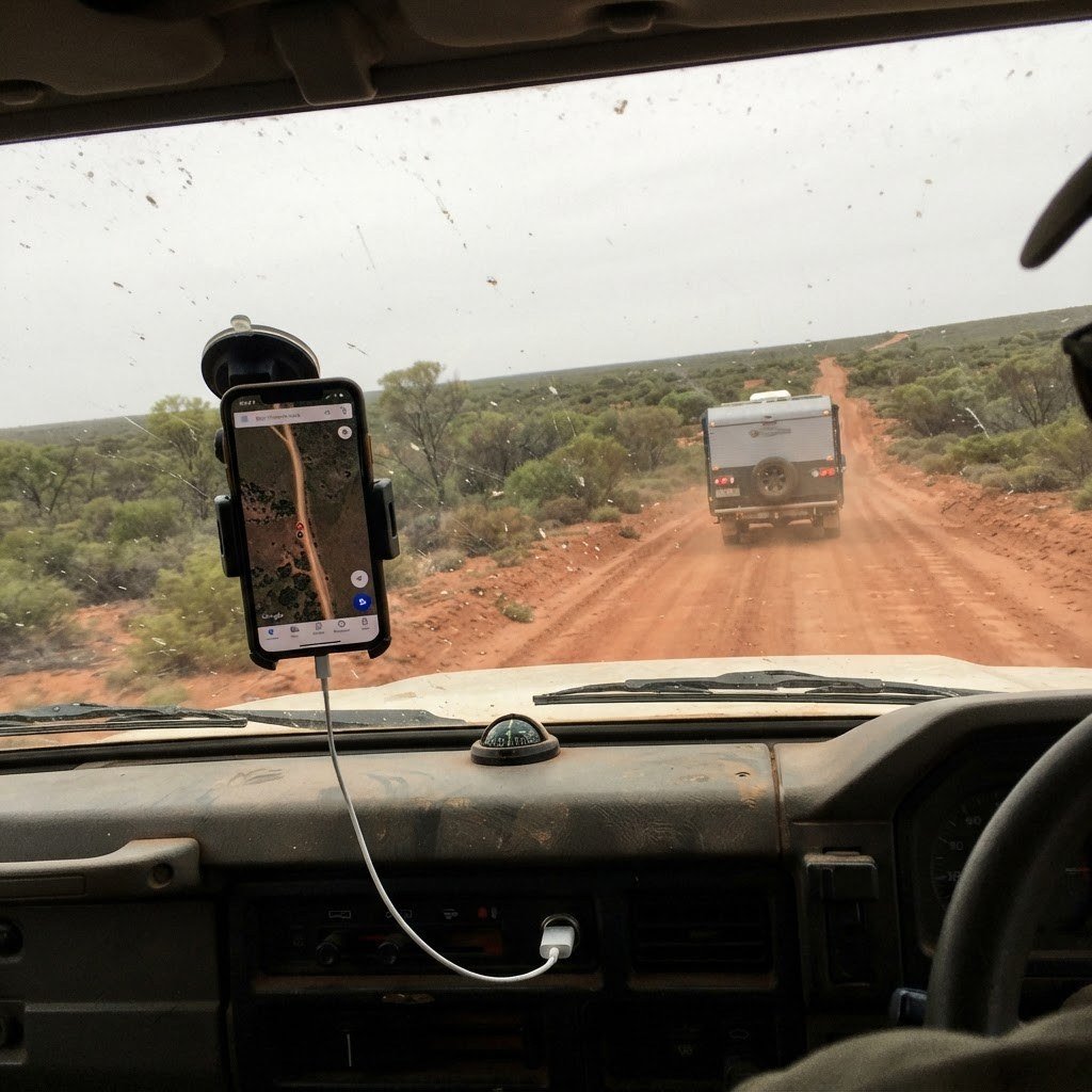 phone in a suction-mount cradle on a dusty 4WD dash with charging cable, outback road ahead